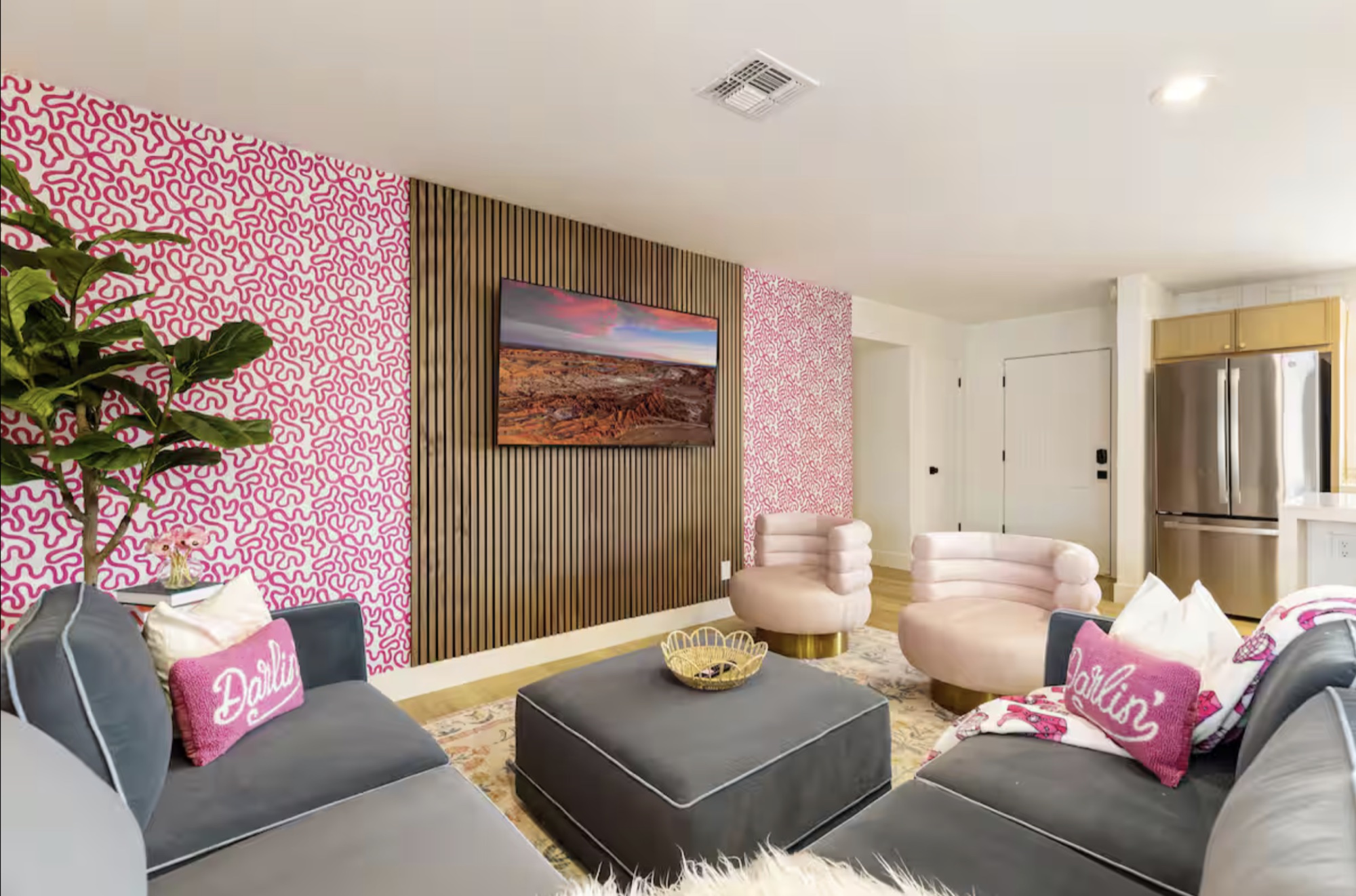 A playful living room with a dark sectional, pale pink chairs, and patterned pink wallpaper at Cowgirl Cottage