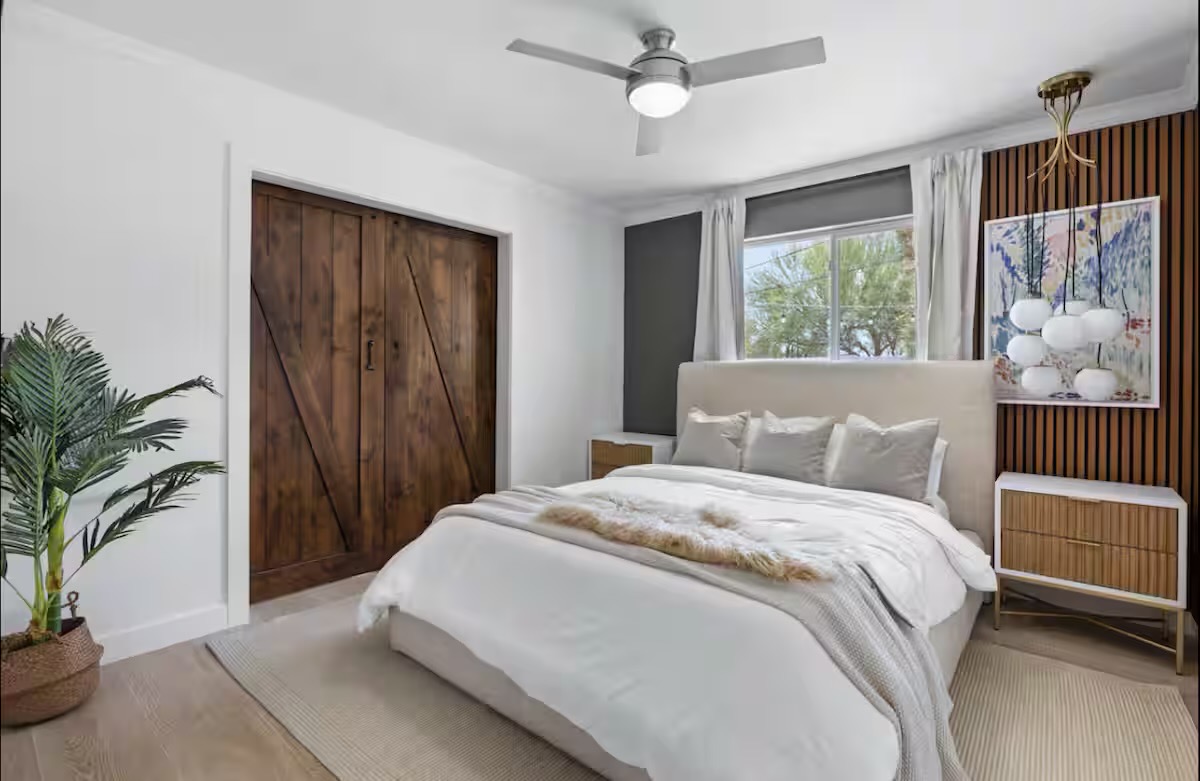 Bedroom with an upholstered cream bed, timber slat accent wall, globe-cluster brass pendant, fluted-wood nightstands, and dark plank barn-style closet doors.